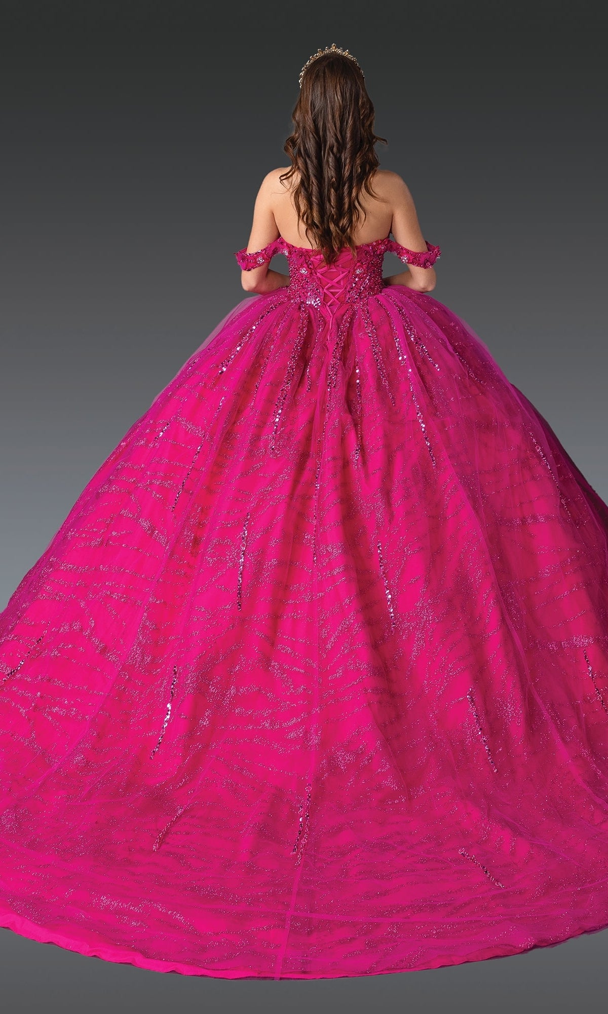 A woman stands with her back to the camera in the Hot Pink Quinceanera Dress 1957 By Dancing Queen, a strapless ball gown with a corset bodice and sparkling details, set against a gray background.